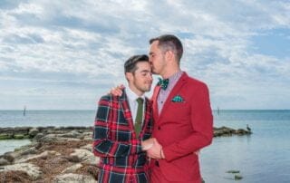 Two men in red suits sharing a tender kiss on the beautiful beach of Key West, captured by a skilled wedding photographer specializing in Key West weddings.