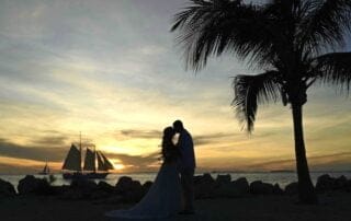 A bride and groom share a romantic kiss on the beach at sunset during their Key West wedding ceremony.