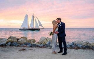 A bride and groom share a passionate kiss in front of a sailboat at sunset, captured beautifully by a talented Key West wedding photographer.