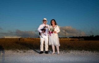 A man and woman, dressed in attire perfect for a key west wedding, standing on a dirt road with a dog.