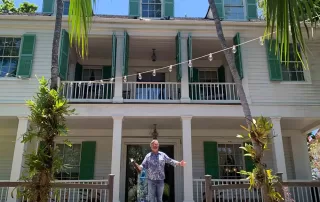 A man standing in front of a house with green shutters, providing key west wedding packages.