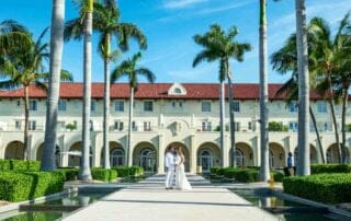 A bride and groom standing in front of a mansion with palm trees, captured beautifully by a Key West wedding photographer.