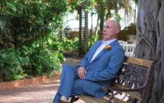 A man in a suit sitting on a bench under a tree, captured by a talented key west wedding photographer.