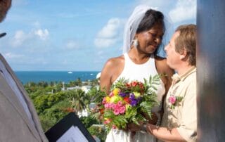 A couple exchanges vows on a balcony overlooking the ocean.