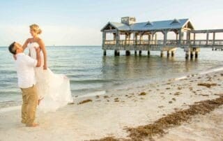 A bride and groom exchanging vows on the beach near a pier, with the assistance of knowledgeable Key West wedding planners.