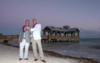 Two men standing on the beach in front of a pier captured by a Key West wedding photographer.