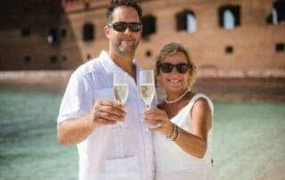 A couple holding champagne glasses on the beach, celebrating their Key West wedding.