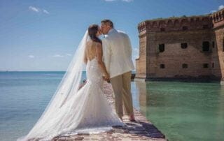 A bride and groom share a kiss in front of an old fort during their Key West wedding.