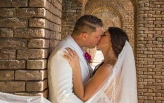 A bride and groom share a passionate kiss in front of a beautifully decorated archway at their Key West wedding ceremony.