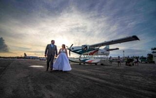 A bride and groom, captured by a talented Key West wedding photographer, joyfully stand in front of a small plane during their unforgettable Key West wedding ceremony.