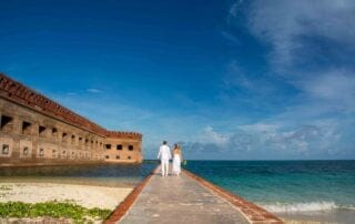 A bride and groom standing on a walkway next to the ocean, captured beautifully by a talented Key West wedding photographer.