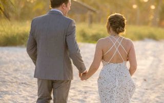 A serene sunrise wedding at Smathers Beach, Key West, featuring a couple exchanging vows on the sandy shore. Palm trees frame the golden sunrise, creating a picturesque and romantic setting. The calm ocean and the soft morning light provide a perfect backdrop for intimate nuptials.