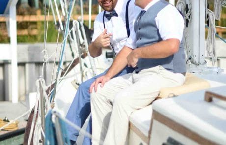 Wedding Two men in semi-formal attire laughing and interacting on a sailboat, with one giving a thumbs-up.