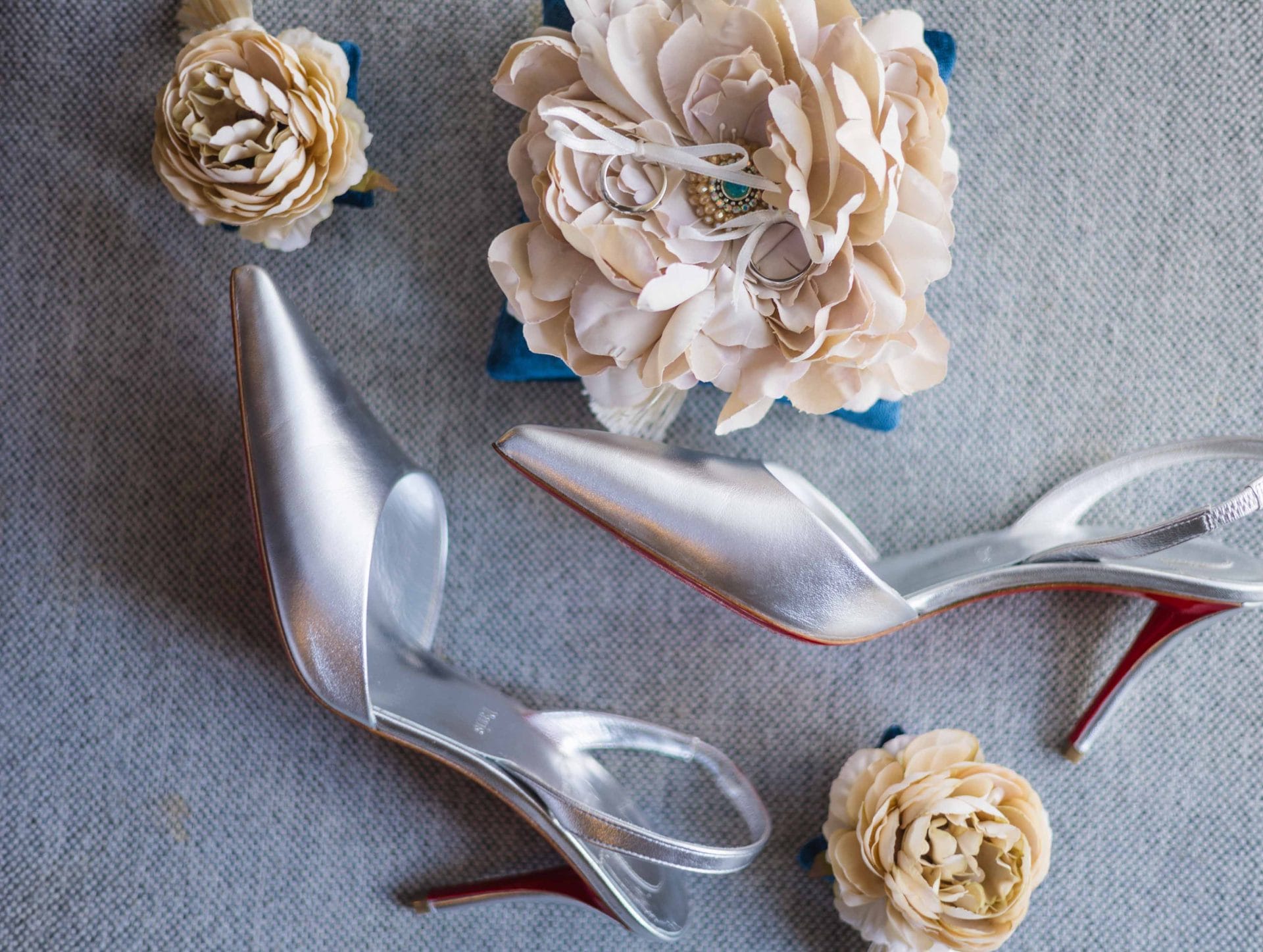 2024-10-29 SOcial media_-9475 Silver high heels and cream flowers are arranged on a gray fabric background.